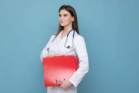Portrait of a young female doctor in a white coat with red folders