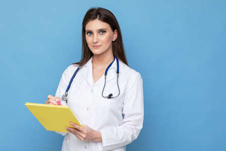 Portrait of a young woman doctor in a white coat writes in the diary