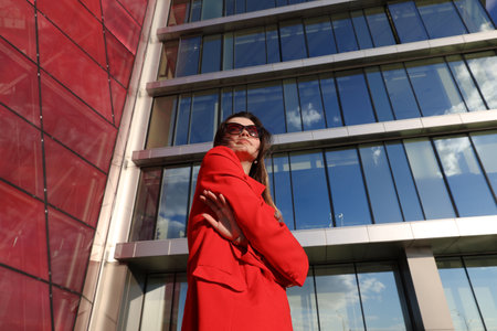 Portrait of a young woman in a red jacket on the background of glass buildings