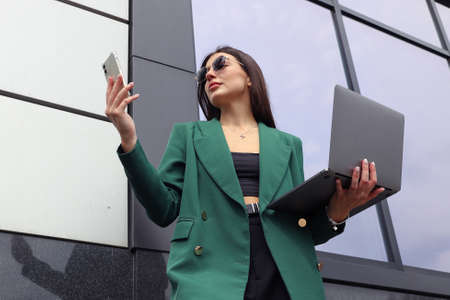 Portrait of a young woman in a business suit with a laptop and a mobile phone