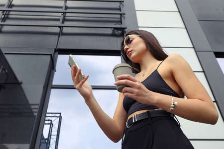 Portrait of a young woman with a mobile phone drinking coffee on the street