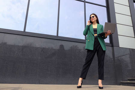 Portrait of a young woman in a business suit with a laptop and a mobile phoneの写真素材