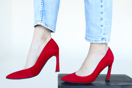 Feet in jeans and red heeled shoes on a white backgroundの写真素材