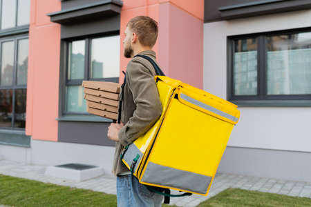 The back of a male courier with a yellow bag during pizza delivery