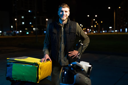 Evening portrait of a male courier on a scooter. Round-the-clock food delivery