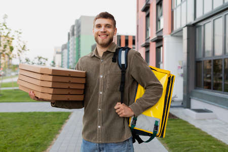 Smiling courier man with pizza in his hands against the backdrop of the urban landscapeの写真素材