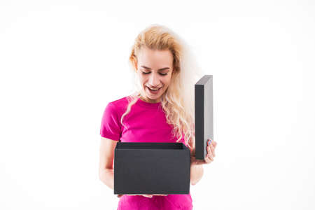 A surprised young woman looks into a gift box. Emotional portrait on a white background