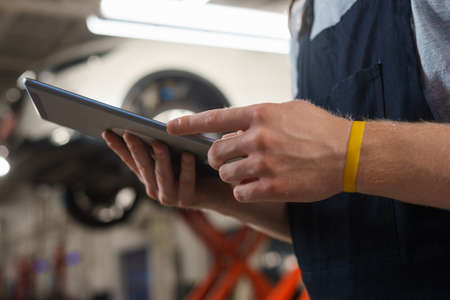 Close-up of the hands of a male car mechanic with a tablet in his hands. A service station employee writes down the work doneの写真素材