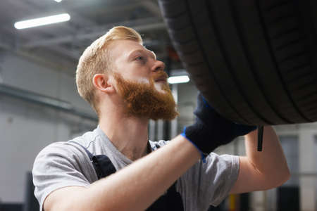 Portrait of a male car mechanic who checks the braking system of a car on a lift in a service...