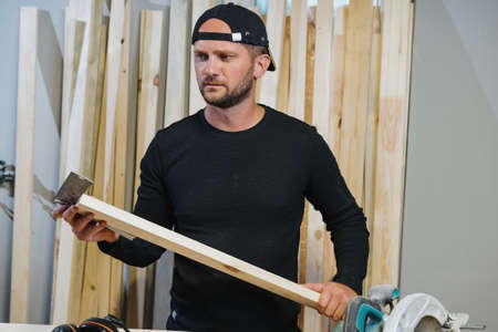 A male carpenter measures the evenness of the board with an angular ruler. A woodworker in his workshopの写真素材