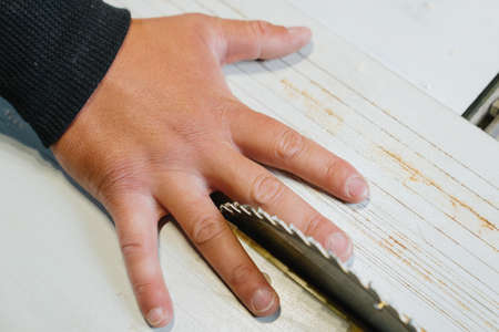 The carpenter's hand lies at the cutting disc of the circular saw. The concept of the danger of...