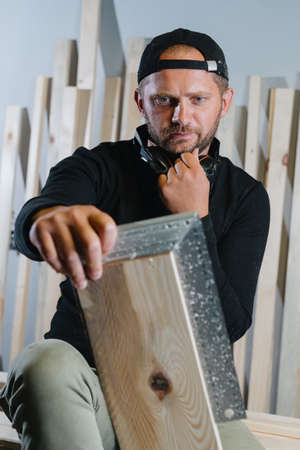 A man carpenter with a beard in dark clothes measures the boards with a ruler before creating a new productの写真素材