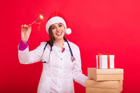 The doctor congratulates the clinic's patients on Christmas and New Year. Young woman with gift boxes on a red backgroundの写真素材