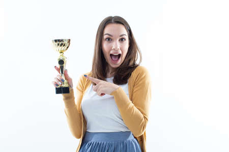 A young woman holds the winner's gold cup on a white background. Emotional portrait of the modelの写真素材