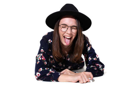 A young woman in a hat is lying on a white background. Stylish model makes a face at the camera in the studioの写真素材