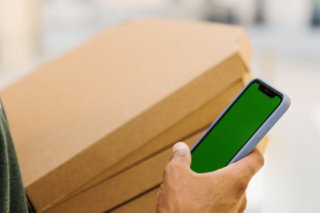 Chroma key on the phone. Close-up of the hands of an African-American pizza delivery man who holds a...