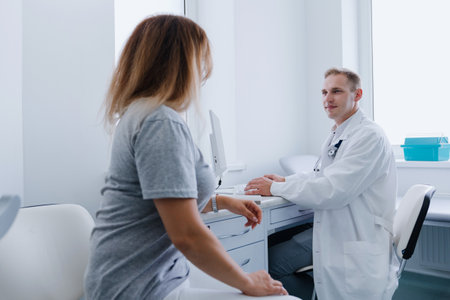 A woman at a doctor's appointment. The male doctor listens attentively to the patient and writes the treatment plan into the computer.の写真素材