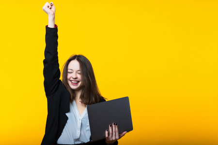 A successful decision in business. Portrait of a young woman with a laptop on a yellow background.の写真素材