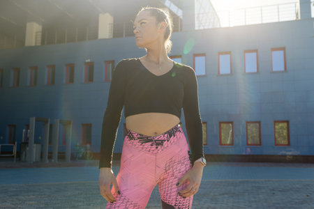 Portrait of a young athletic woman in bright leggings and a black top posing against the background...
