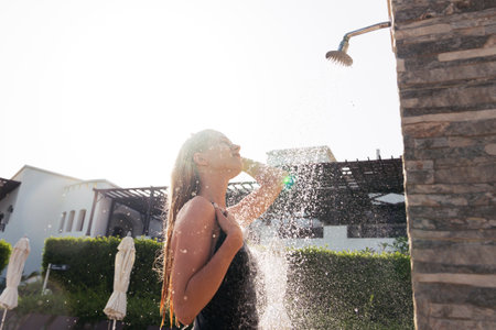 A young woman in a black swimsuit takes a shower after swimming in the poolの写真素材