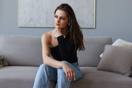 Fashion portrait of a young woman in a black T-shirt and jeans at homeの写真素材