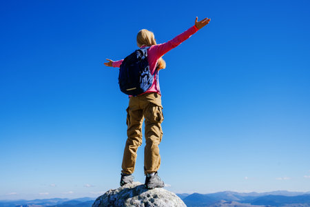 Silhouette of a female tourist with a backpack who enjoys the mountain peaks standing on a cliff....