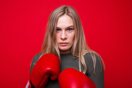 Portrait of a young woman in boxing gloves on a red background. sports and healthの写真素材