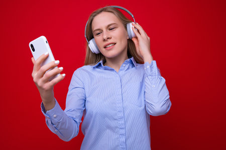 A young woman in a shirt listens to music from her phone on a red backgroundの写真素材