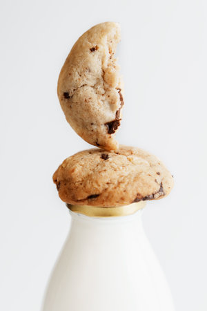 Cookies with pieces of chocolate lying on a bottle of milk on a white backgroundの写真素材