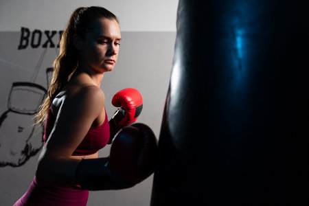 A young woman hits a punching bag with gloves