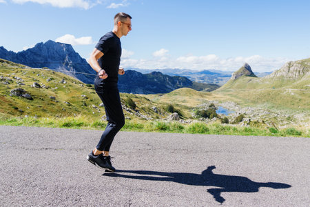 An athletic man does sports outside. A man jumps on a rope on the background of a mountain...