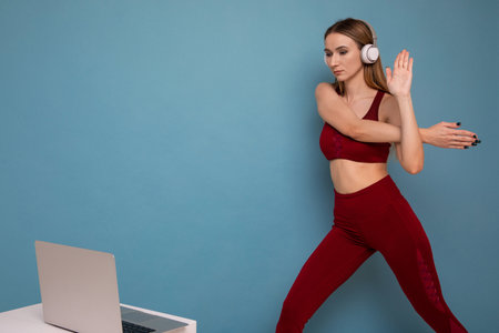 A young woman trains with a trainer online. The model looks at the laptop screen. Sports training during the pandemicの写真素材