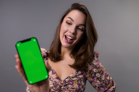 A young woman looks at the mobile phone screen with surprise. The green screen on the smartphone. Placement of ads in applicationsの写真素材