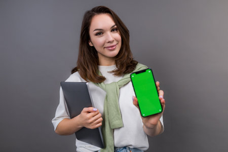 Portrait of a student with a laptop and a mobile phone. The model holds a smartphone with a chroma...