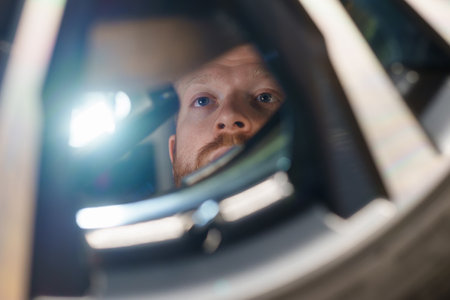 Close-up of the face of a male car mechanic who inspects the braking system of a car with a flashlight at a service stationの写真素材