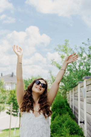 A young woman in a white dress and sunglasses enjoys the summer weather posing on the outsideの写真素材