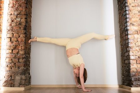 A young woman stands on her hands during a workout. Woman is doing stretching at a yoga school