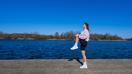 A young woman in a tracksuit is warming up outside.Training on the embankment of the reservoirの写真素材