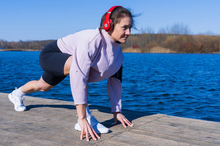A young athletic woman listens to music and trains outdoors
