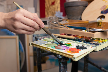 Close-up of the artist's hand with a brush and multicolored paintsの写真素材