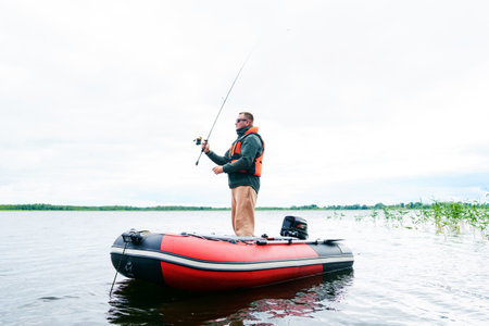 A thirty-year-old man in glasses and a safety vest catches a fish from a boatの写真素材