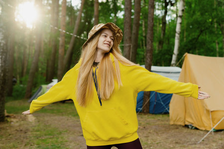 The pleasure of outdoor recreation. A young female tourist in the forest against the background of tentsの写真素材