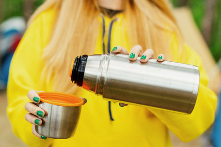 Close-up of a woman's hands with a tumbler in nature. Morning coffee on a hikeの写真素材