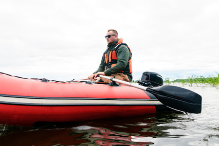 A view from the water of a fisherman sitting in a boat and rowing with oarsの写真素材