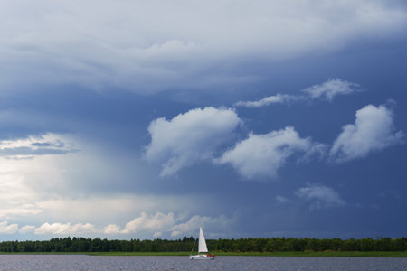 A sailboat floats on the waves against the background of the shore. cloudy skyの写真素材