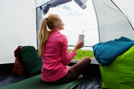Tent camp. A young woman enjoys nature. Rest in a tent. Hiking, camping, active lifestyleの写真素材