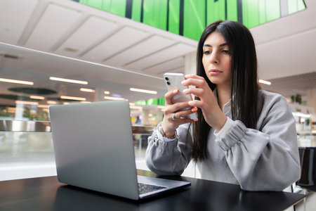 Remote work from a cafe in a shopping center. A young woman types on her phone while working