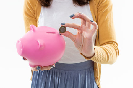 An unrecognizable woman puts a coin in a piggy bank. The concept of saving moneyの写真素材