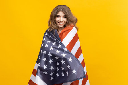 This photo captures the strength and beauty of an American woman as she holds the flag with grace and poise against a vibrant yellow backdropの写真素材