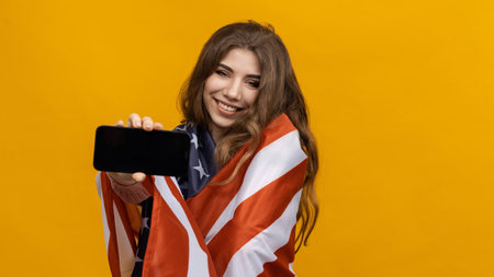 An American woman with a smartphone in her hands looks into the camera. yellow studio background. The concept of IT technologiesの写真素材